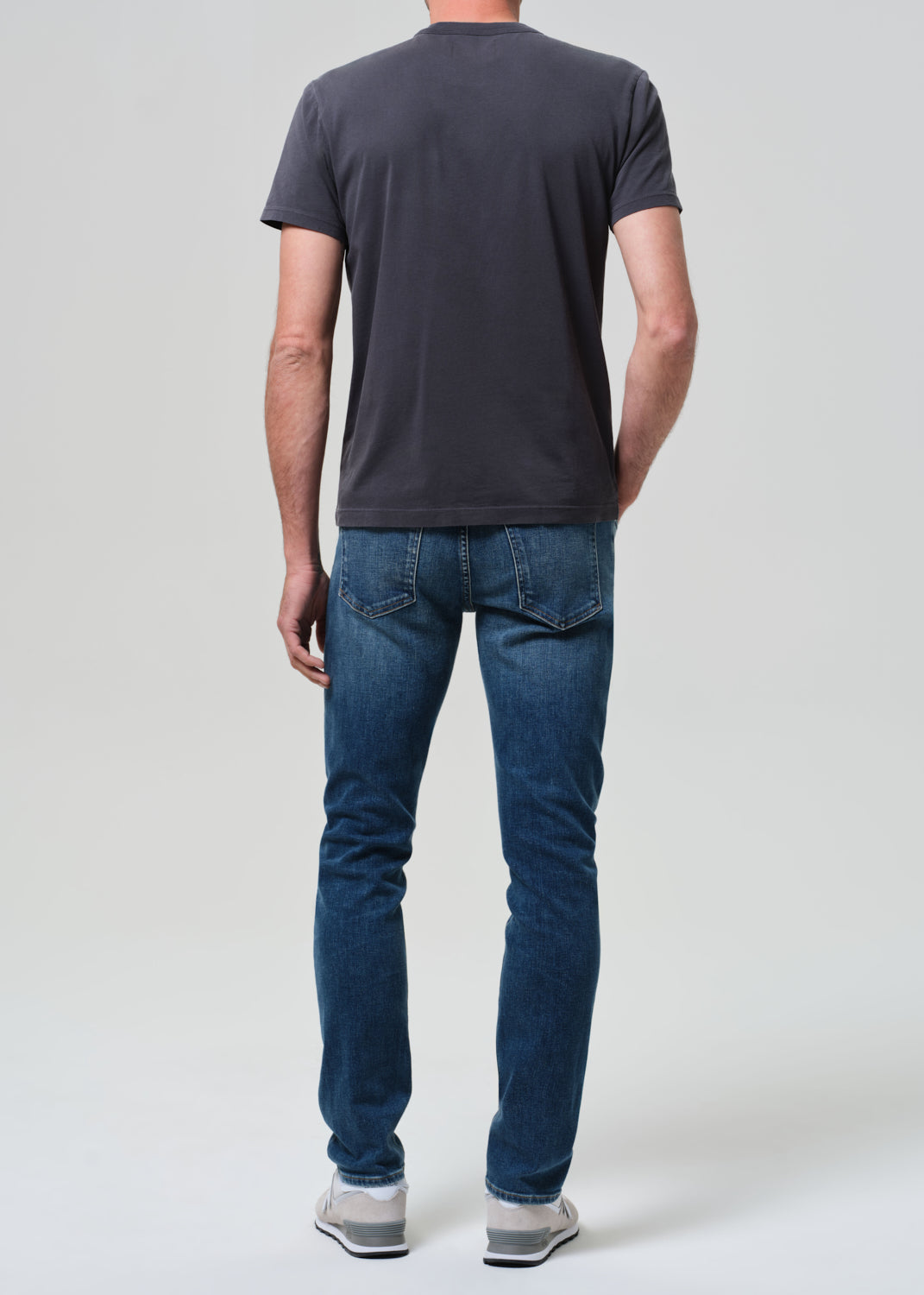 Person wearing a dark gray t-shirt and blue jeans on a white background