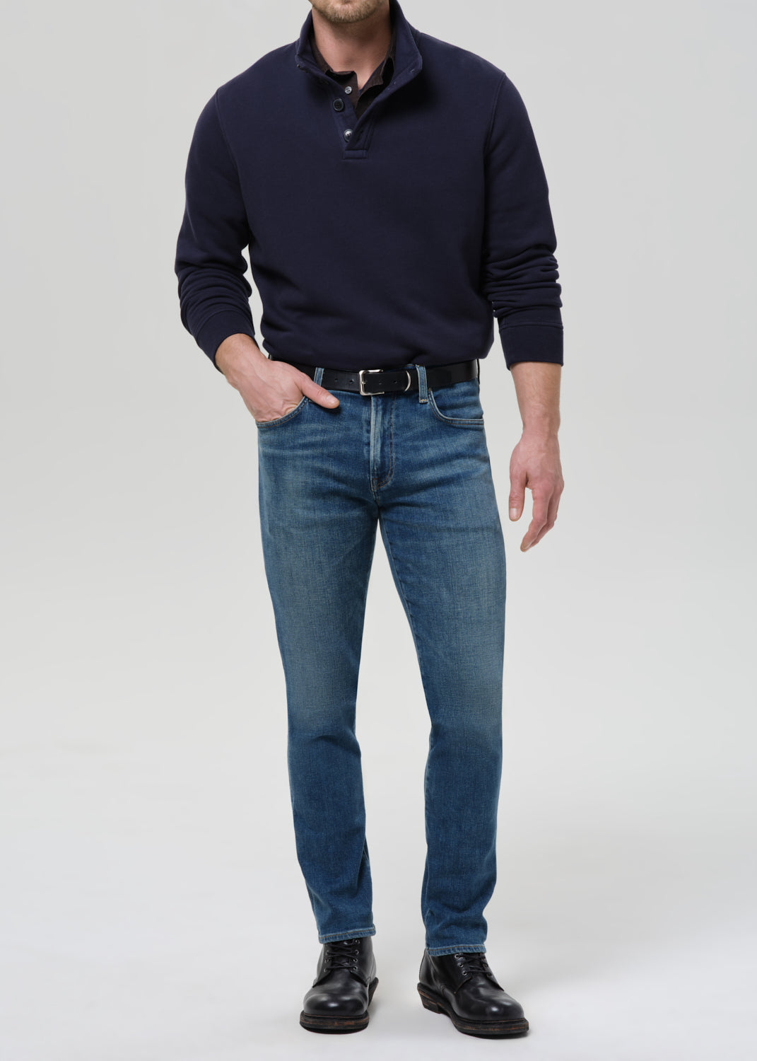 Man wearing a navy sweater and blue jeans on a grey background.
