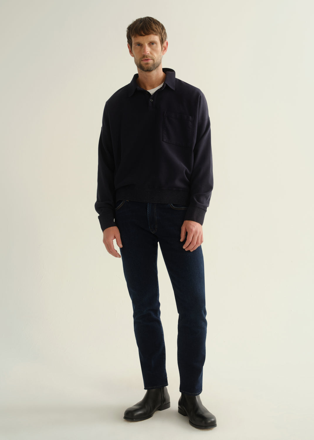 Person wearing a dark navy long sleeve shirt, dark indigo jeans, and black boots, front full body view on a light grey background.