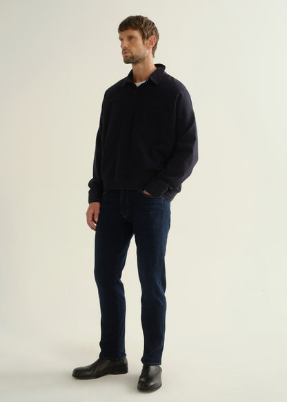 Person wearing a dark navy long sleeve shirt, dark indigo jeans, and black boots, angled front full body view on a light grey background.