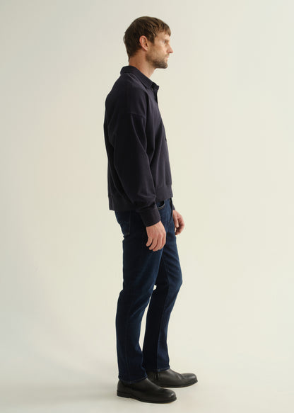 Person wearing a dark navy long sleeve shirt, dark indigo jeans, and black boots, side full body view on a light grey background.