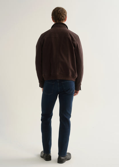 Person wearing dark indigo blue jeans, a dark brown jacket, and black boots, back full body view on a light grey background.