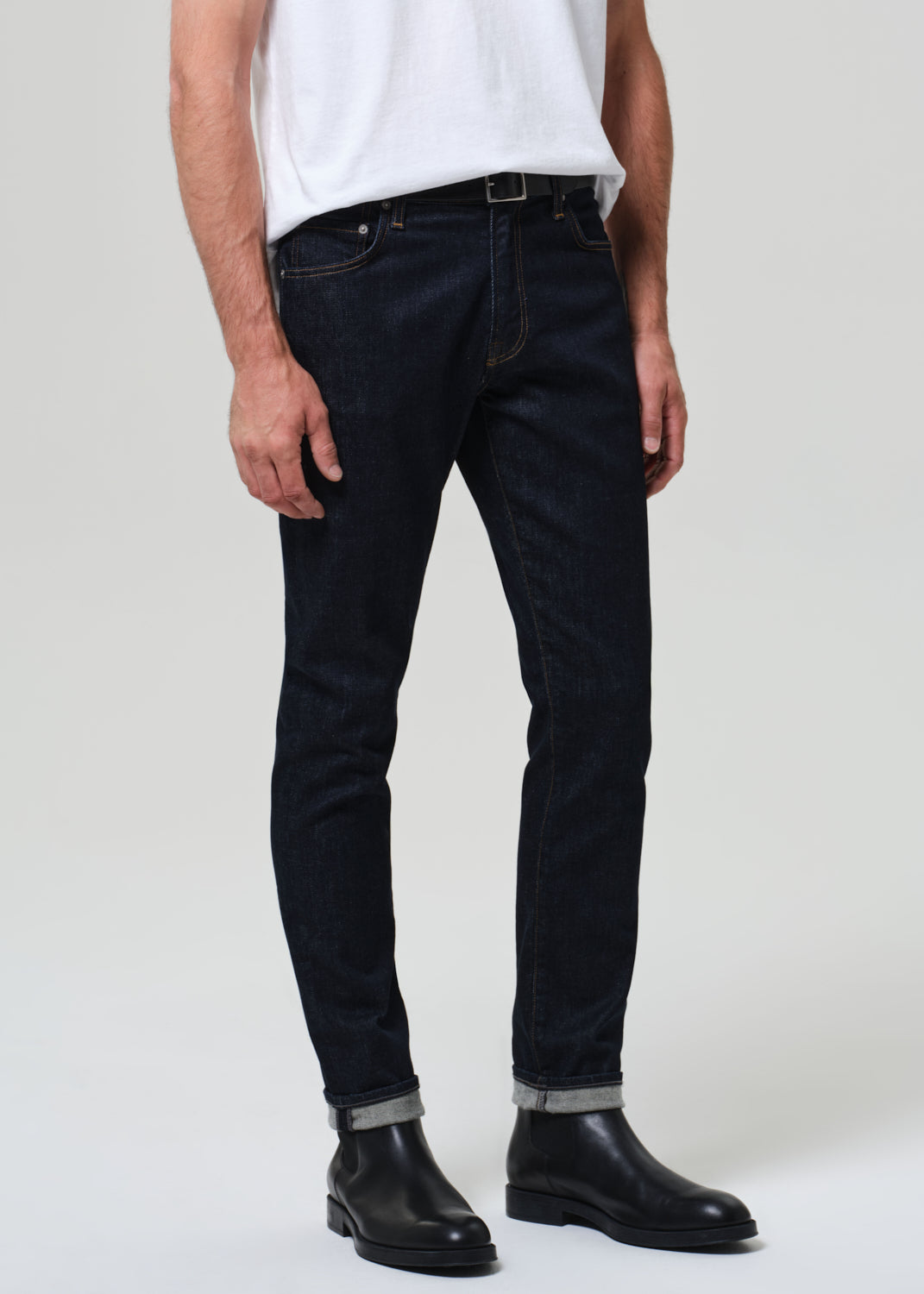 Person wearing dark jeans and black shoes on a white background