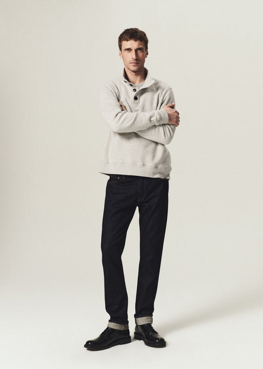 A man modeling a light gray quarter-zip pullover sweater, black trousers, and black leather shoes against a plain light gray studio background.