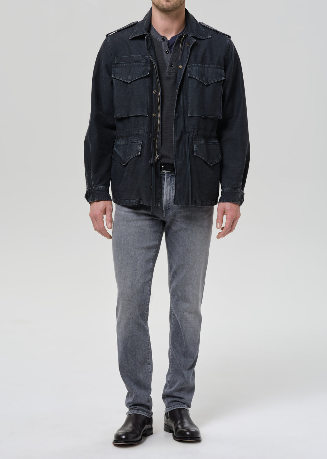 Person wearing light grey straight leg jeans with a black denim jacket and black crewneck tee on a grey background.