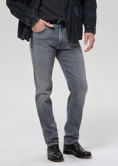 Person wearing light grey straight leg jeans with a black denim jacket and black crewneck tee on a grey background.