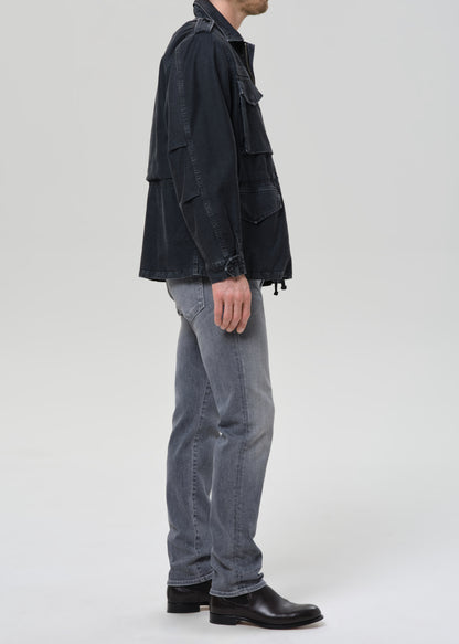 Person wearing light grey straight leg jeans with a black denim jacket and black crewneck tee viewed from the side on a grey background.