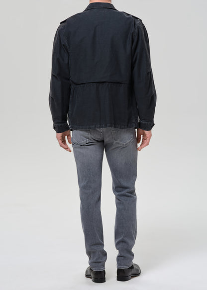Person wearing light grey straight leg jeans with a black denim jacket and black crewneck tee viewed from the back on a grey background.