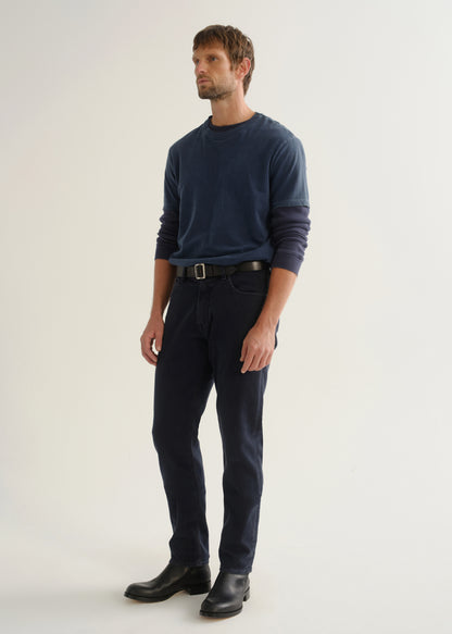 Person wearing dark navy pants, a blue long sleeve shirt, and black boots, angled front full body view on a light grey background.