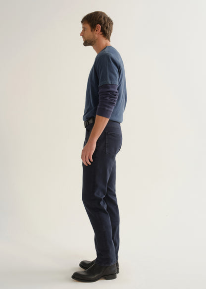 Person wearing dark navy pants, a blue long sleeve shirt, and black boots, side full body view on a light grey background.