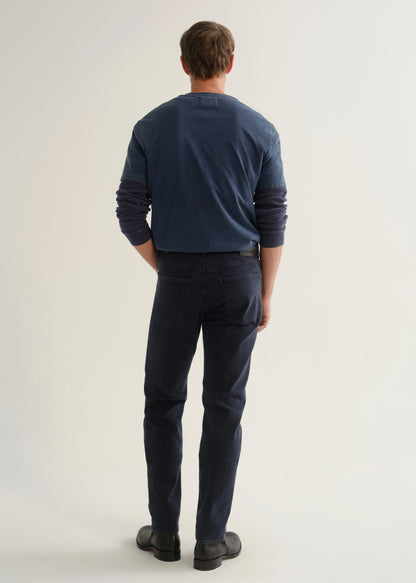 Person wearing dark navy pants, a blue long sleeve shirt, and black boots, back full body view on a light grey background.