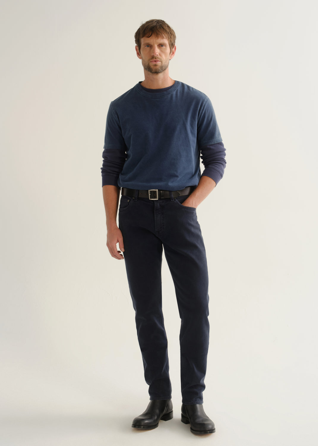 Person wearing dark navy pants, a blue long sleeve shirt, and black boots, front full body view on a light grey background.