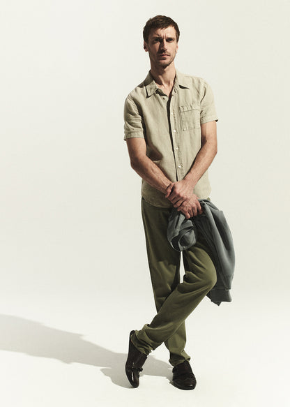 Man wearing a light green shirt and olive pants holding a gray shirt on a white background