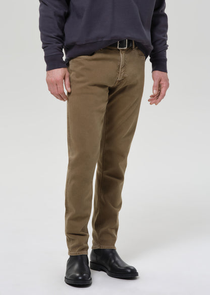 A person wearing slim-fit brown chinos with a dark navy sweatshirt and black leather boots, shown from the chest down against a grey background.