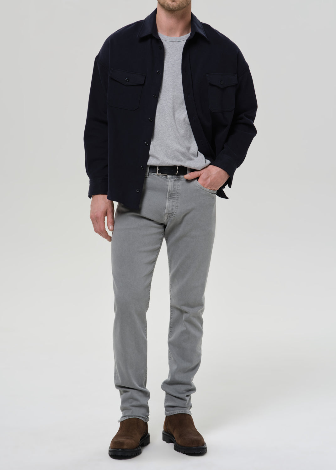 Person wearing a black shirt, grey pants, and brown shoes on a grey background