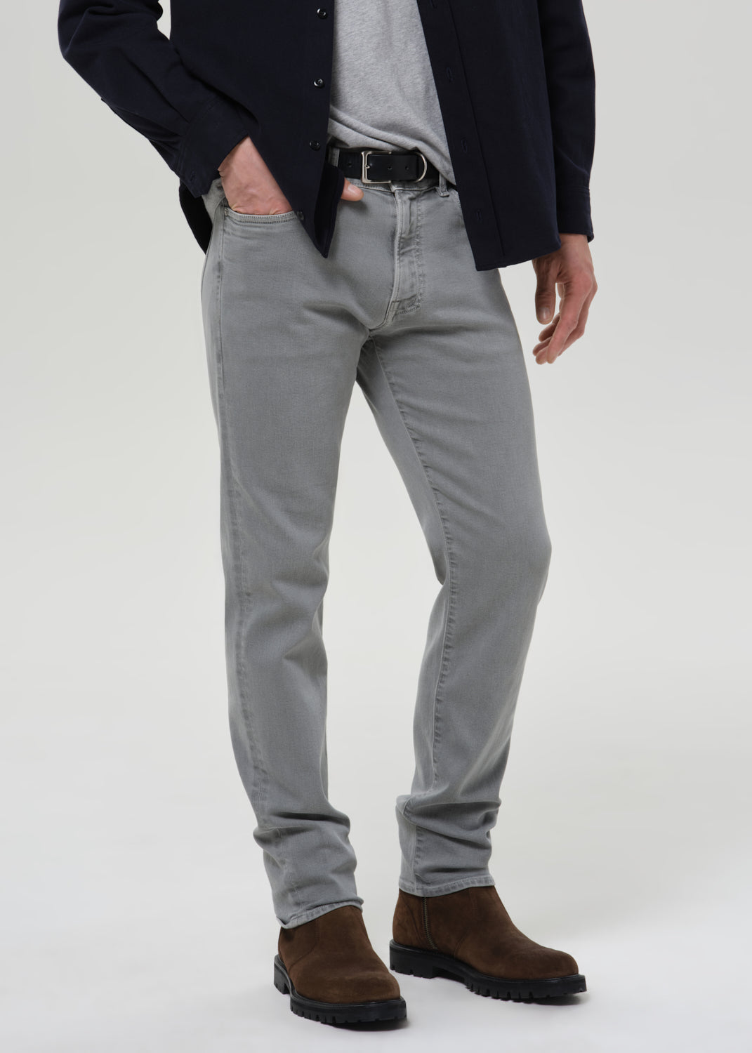 Person wearing grey  jeans and brown boots on a grey background