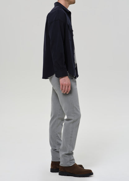 Person wearing a navy jacket, grey  pants, and brown shoes on a grey background