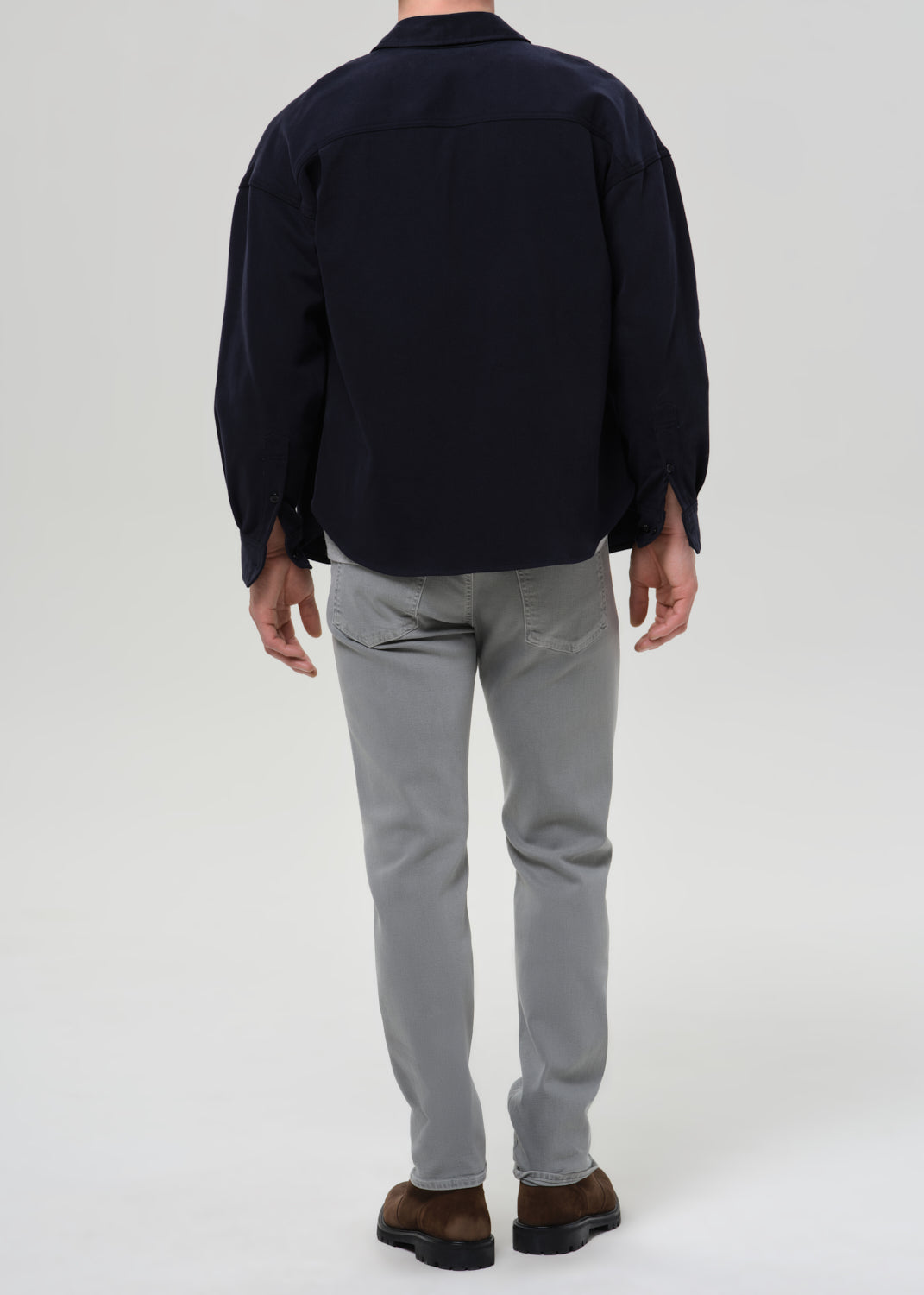 Person wearing a dark shirt and grey pants on a grey background
