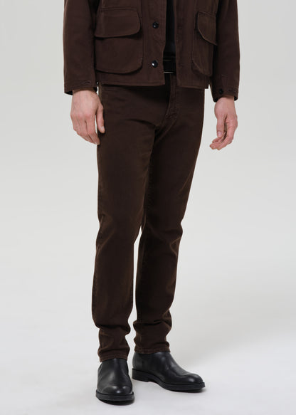 Person wearing a brown jacket and pants with black shoes on a grey background