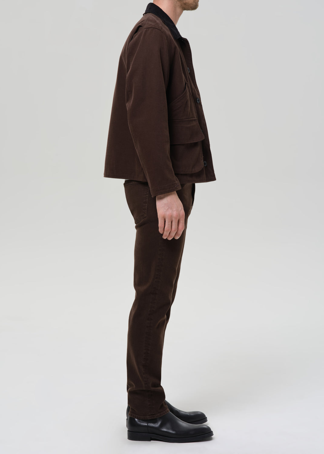 Person wearing a brown jacket and pants on a grey background