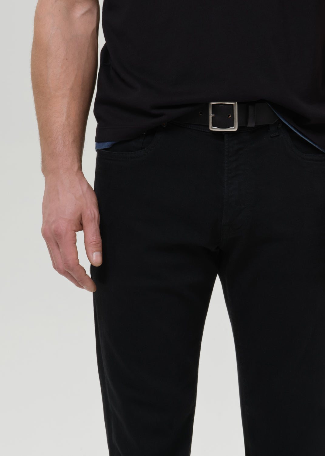 Person wearing black pants with a belt on a grey background
