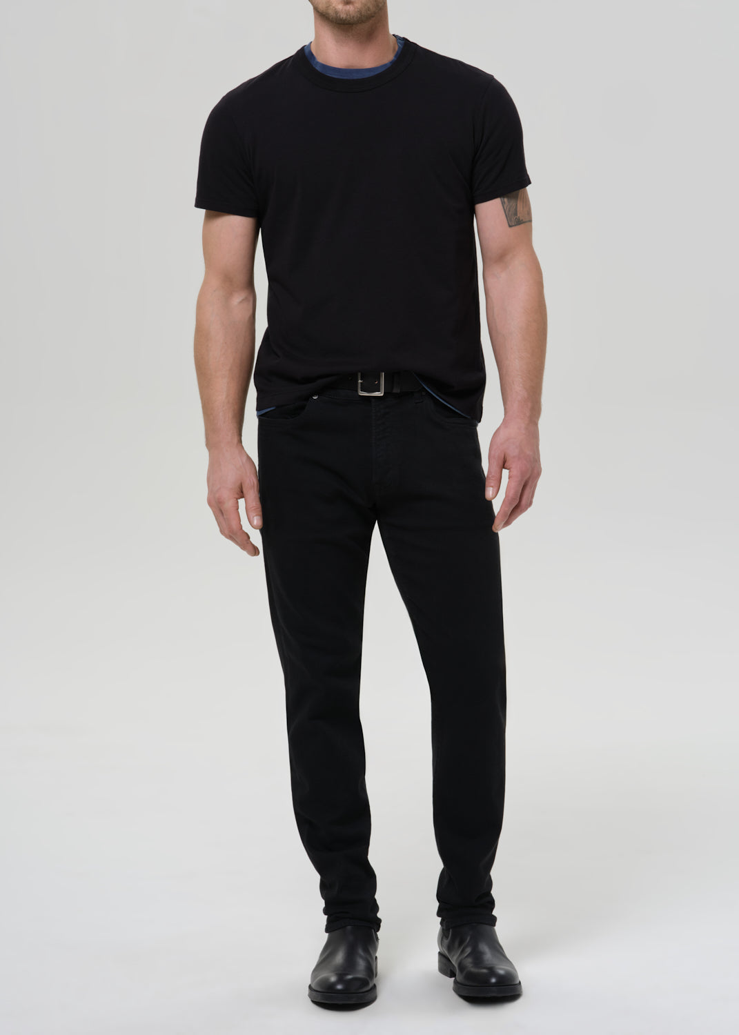 Man wearing a black t-shirt and black pants on a grey background