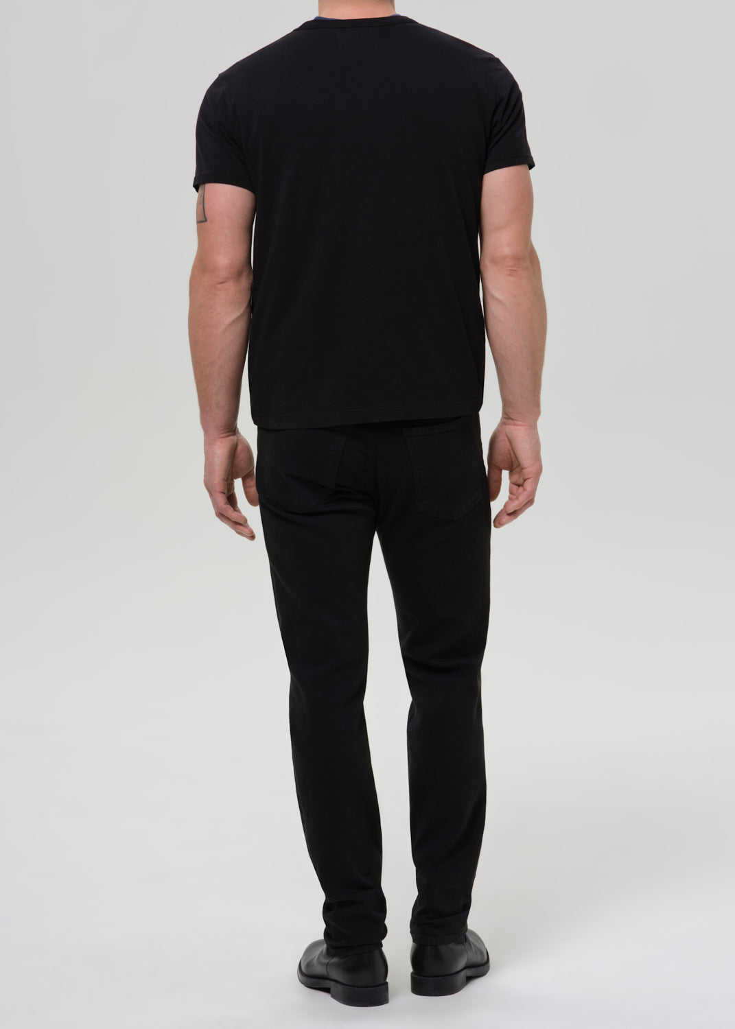 Person wearing a black t-shirt and black pants on a grey background