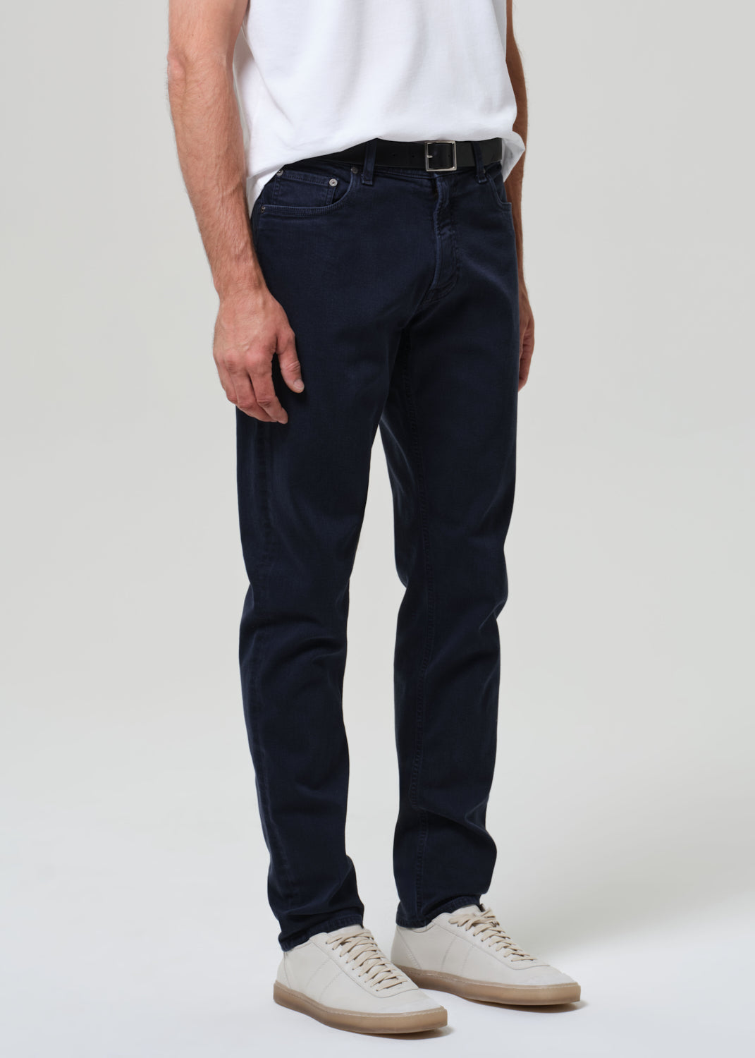 Person wearing navy blue jeans and a white shirt on a plain background