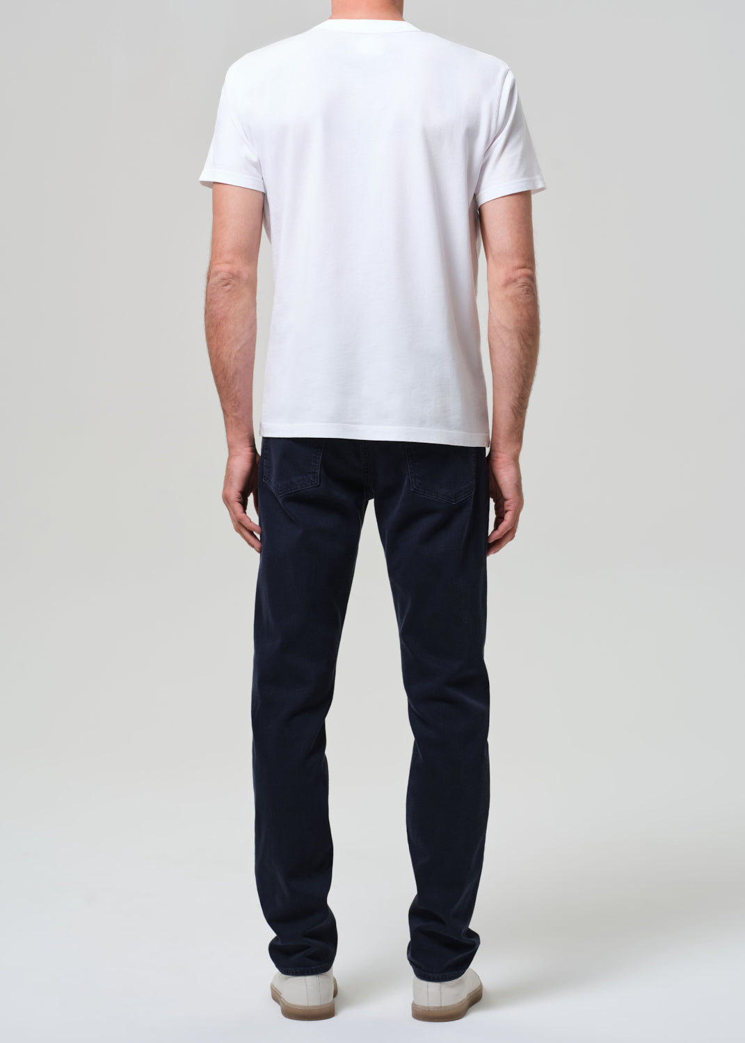 Person wearing a white t-shirt and dark pants on a plain background