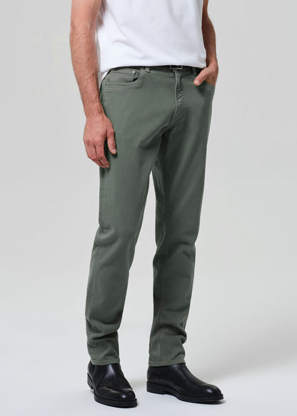Person wearing green pants and black shoes on a plain background