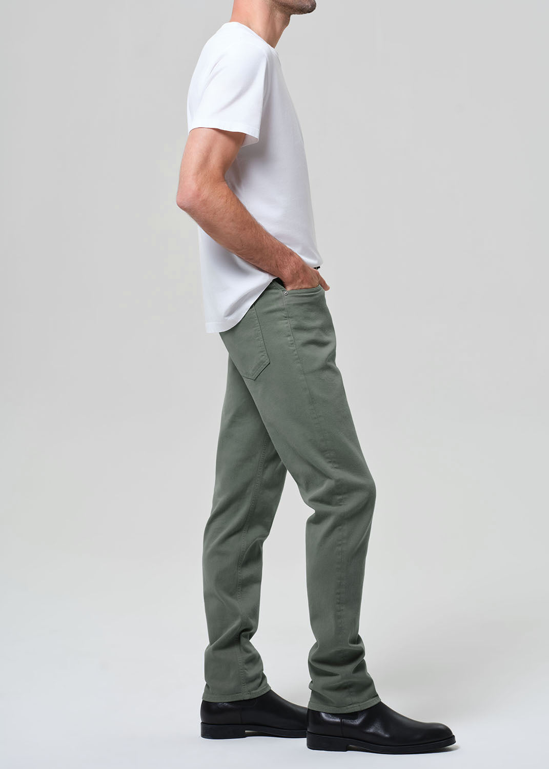 Person wearing green pants and a white shirt on a plain background