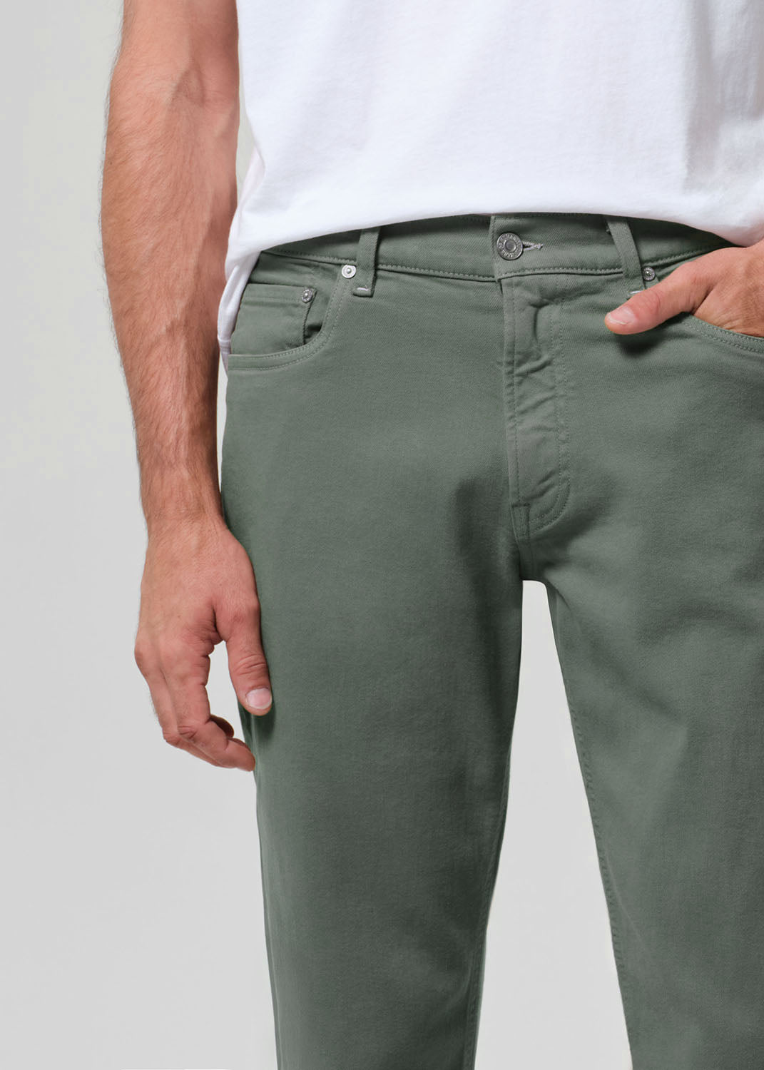 Person wearing green pants and a white shirt on a plain background