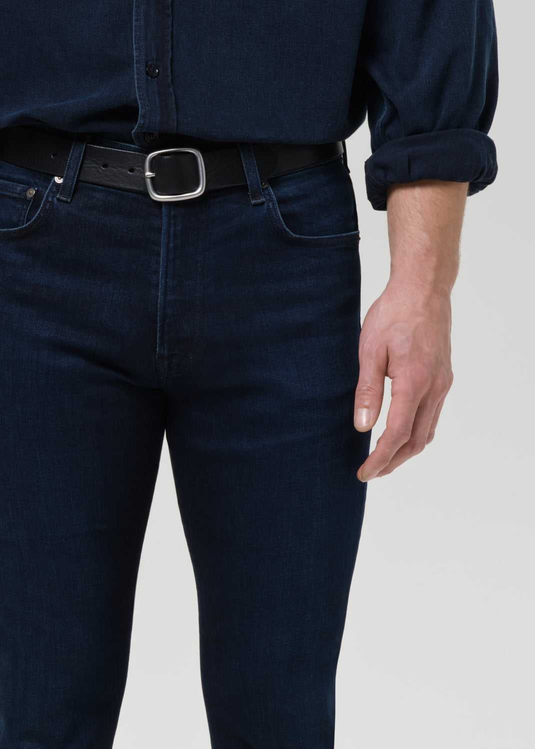 Person wearing dark blue jeans and a matching shirt on a grey background