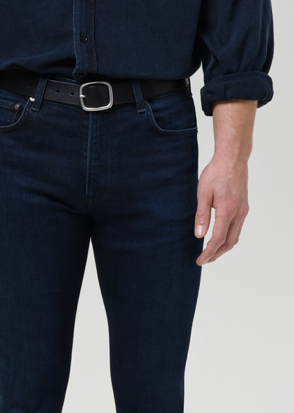 Person wearing dark blue jeans and a matching shirt on a grey background