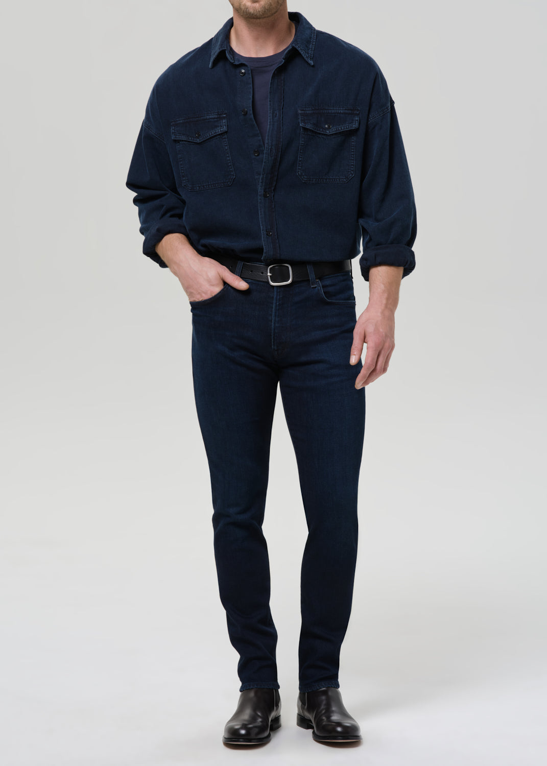 Person wearing a navy blue shirt and blue jeans on a grey background