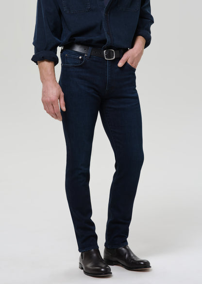 Person wearing dark blue jeans and a matching shirt on a grey background
