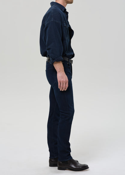 Person wearing a dark blue shirt and blue jeans on a grey background