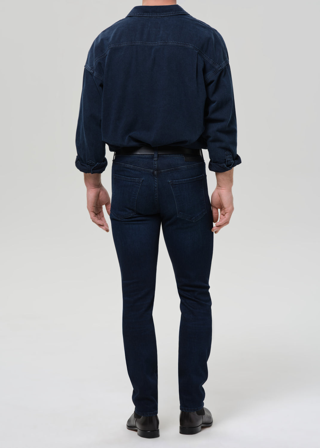 Person wearing a navy blue shirt and blue jeans on a grey background