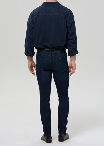 Person wearing a navy blue shirt and blue jeans on a grey background