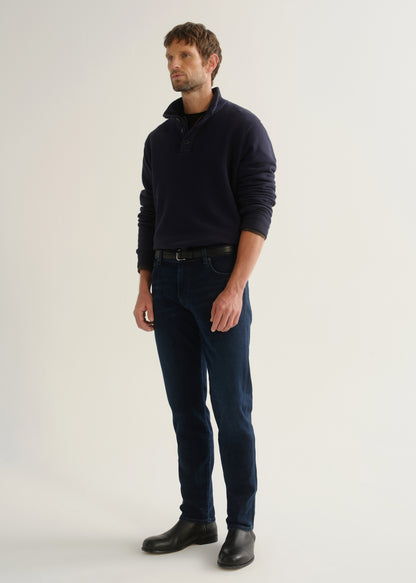 Person wearing dark indigo blue jeans, a navy long sleeve shirt, and black boots, angled front full body view on a light grey background.