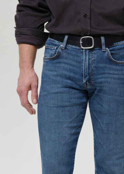 Close-up of medium blue straight leg jeans on a grey background.