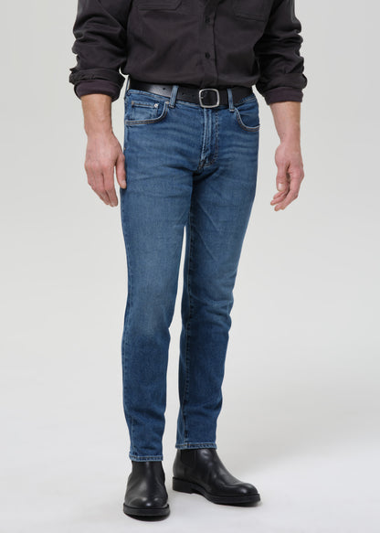 Person wearing medium blue straight leg jeans with a black button-up shirt on a grey background.
