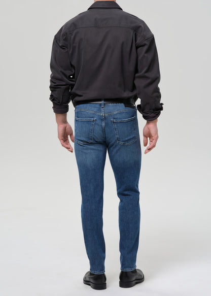 Person wearing medium blue straight leg jeans with a black button-up shirt viewed from the back on a grey background.