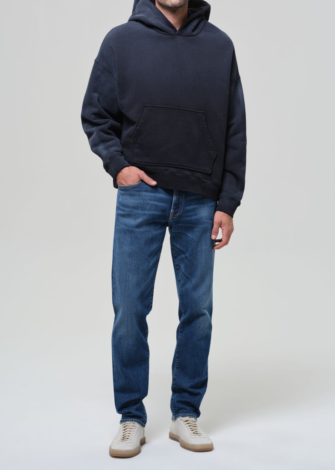 Person wearing a hoodie and blue jeans on a grey background