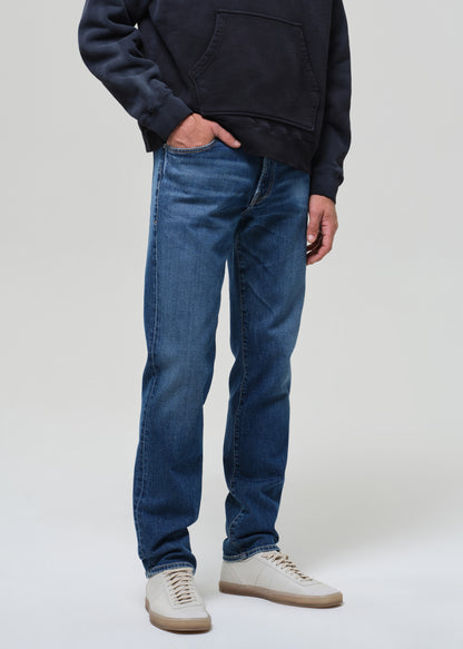 Person wearing a hoodie and blue jeans on a grey background