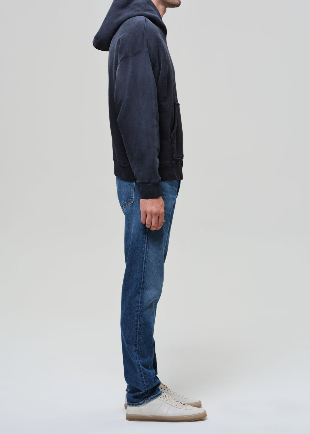 Person wearing a hoodie and blue jeans on a grey background