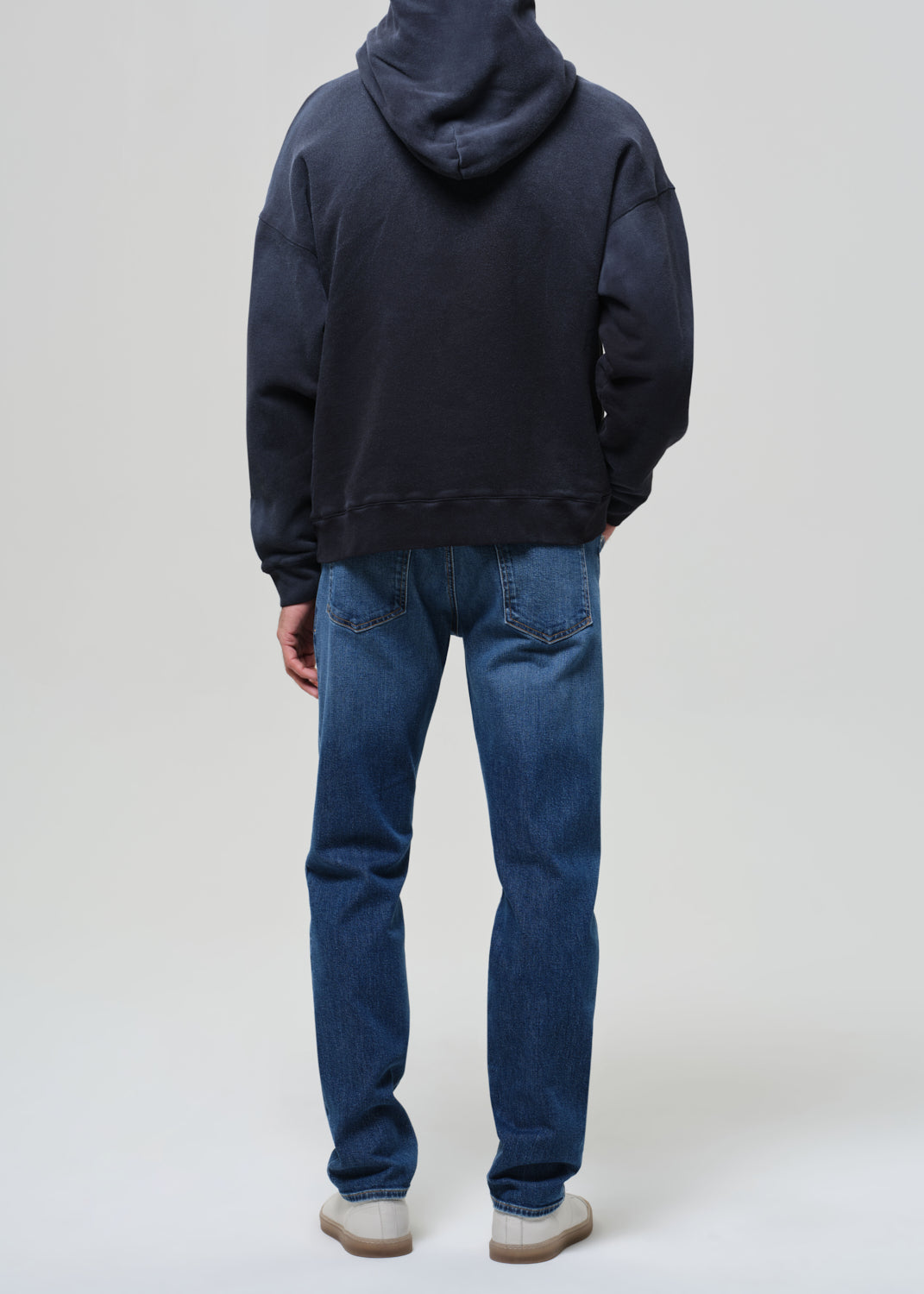 Person wearing a hoodie and blue jeans on a grey background