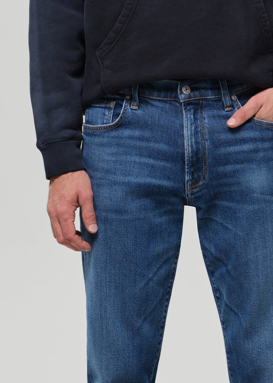 Person wearing a hoodie and blue jeans on a grey background