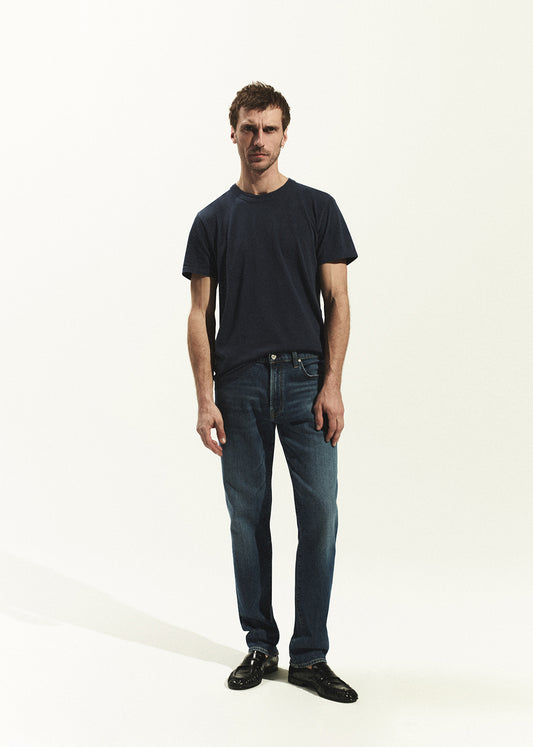 Man wearing a navy t-shirt and blue jeans on a white background