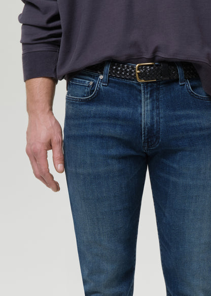 Person wearing blue jeans with a belt on a grey background